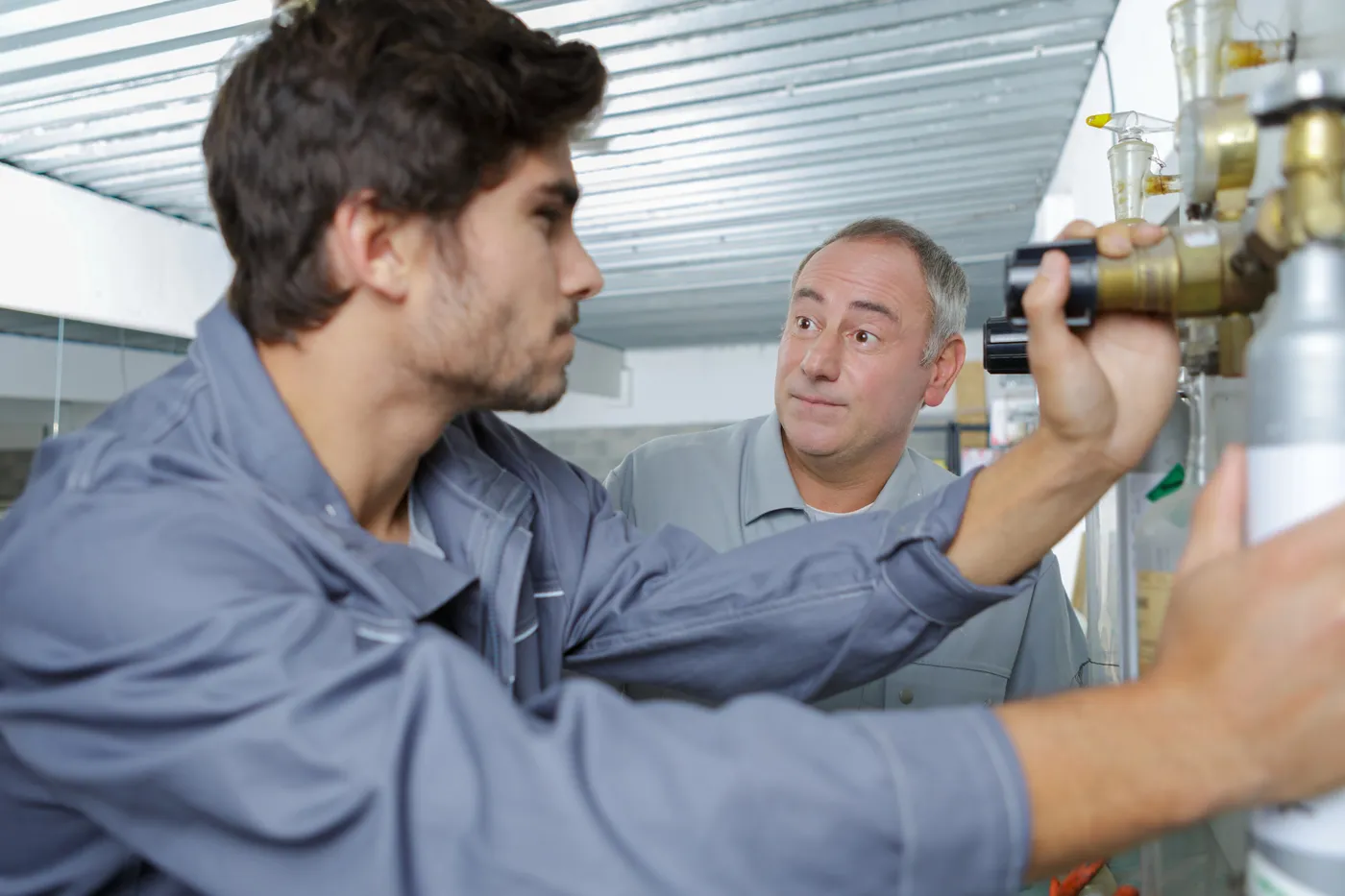 An experienced plumber showing a new trainee the pipework